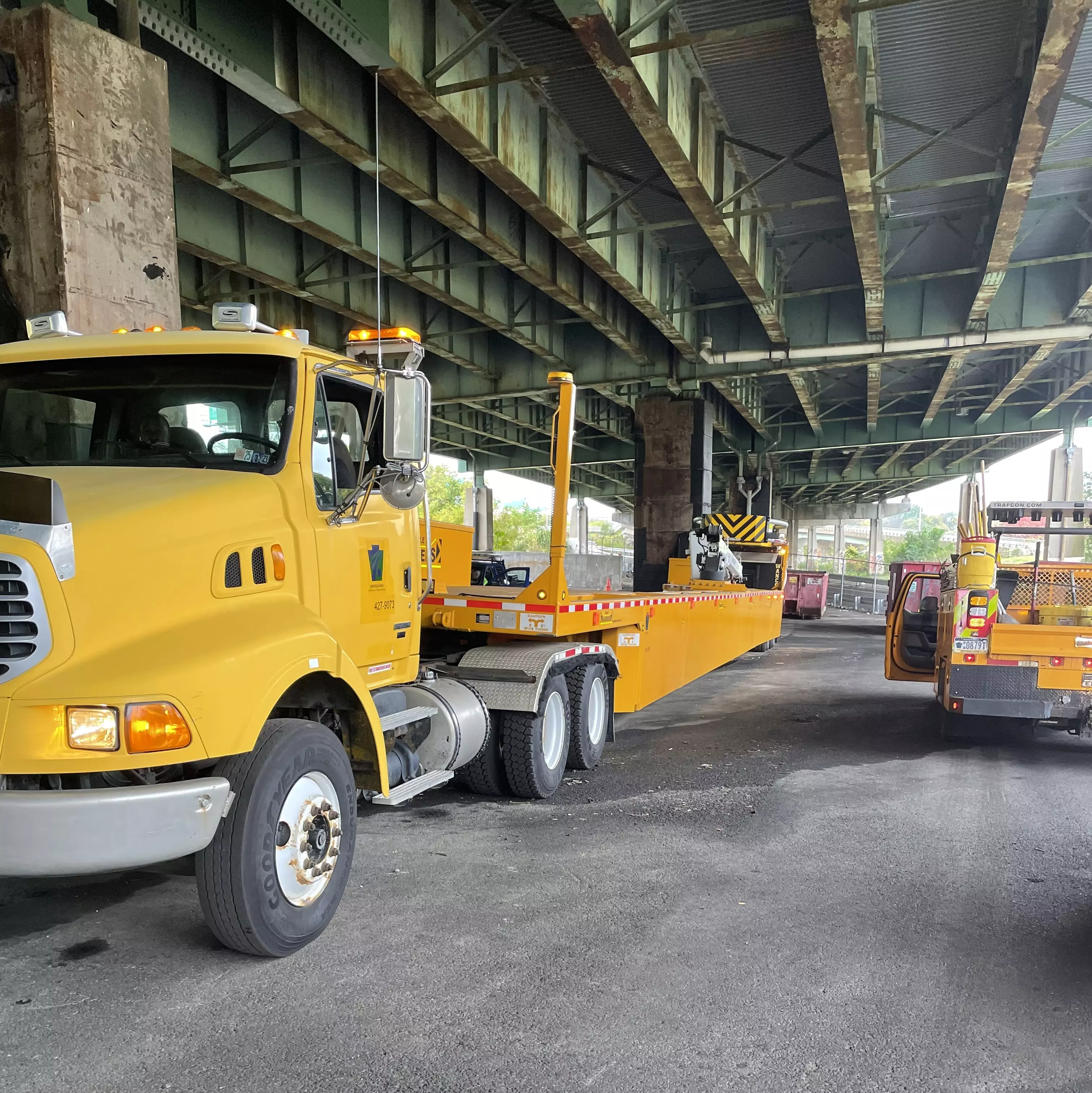 An image of a 110-foot-long yellow mobile truck barrier parked under a bridge overpass.